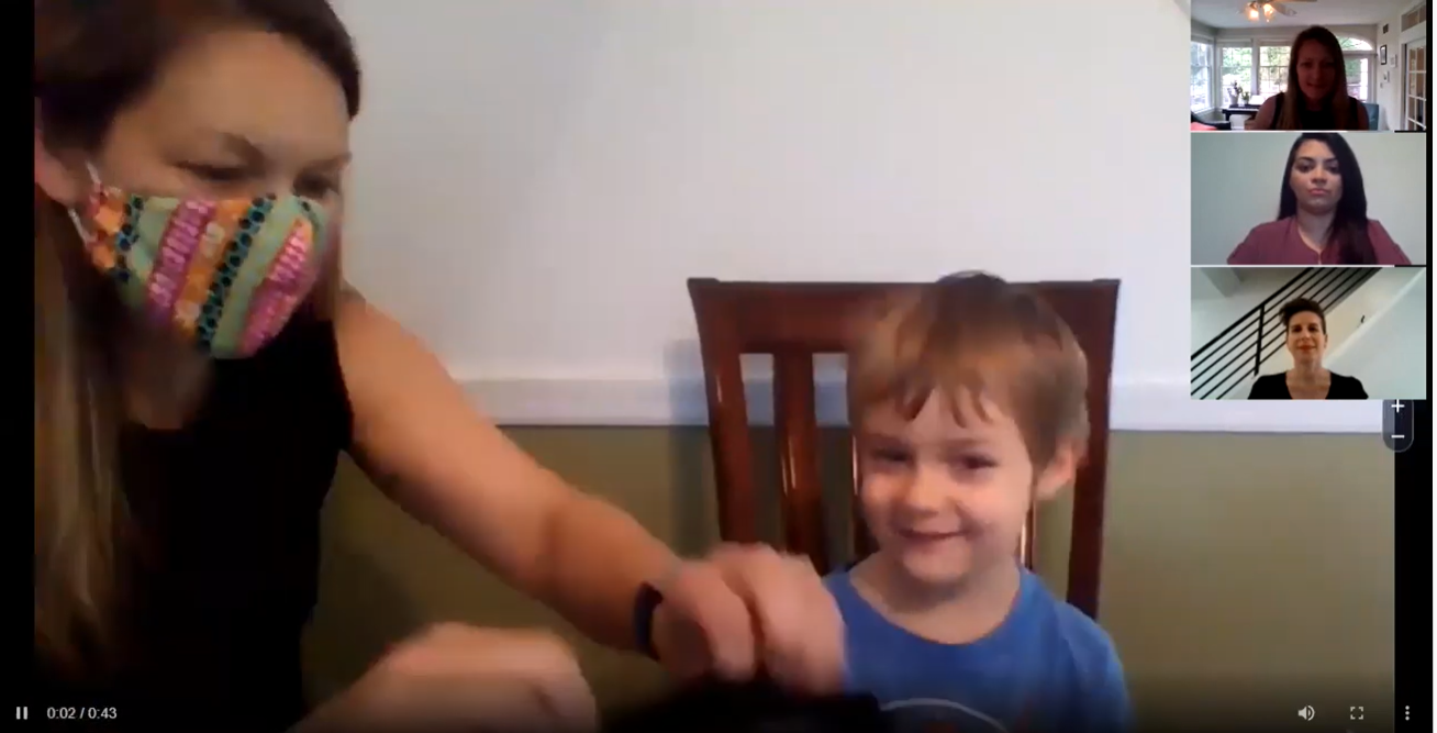 A woman in a mask sits with a young blonde boy on a zoom call with three other women