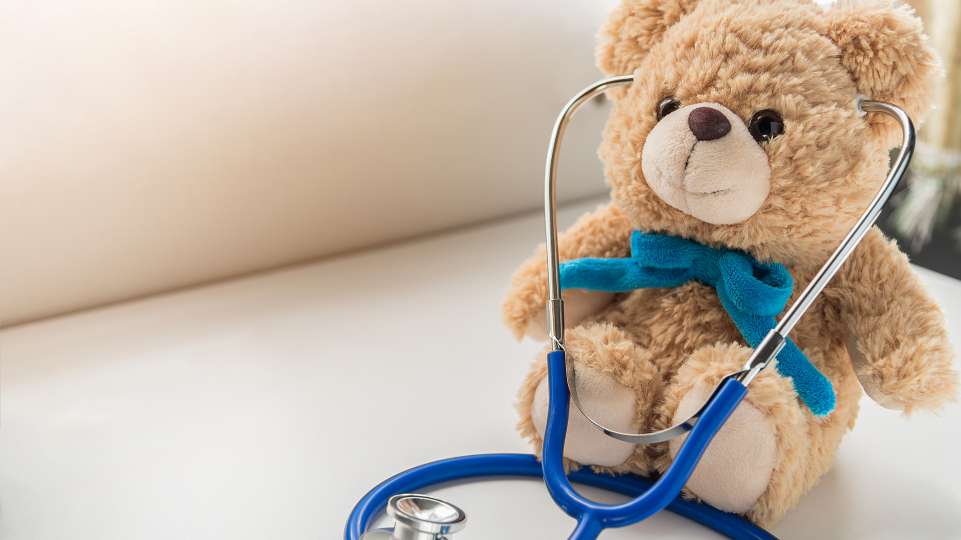 a brown teddy bear with a blue bow sits on a table wearing a stethoscope