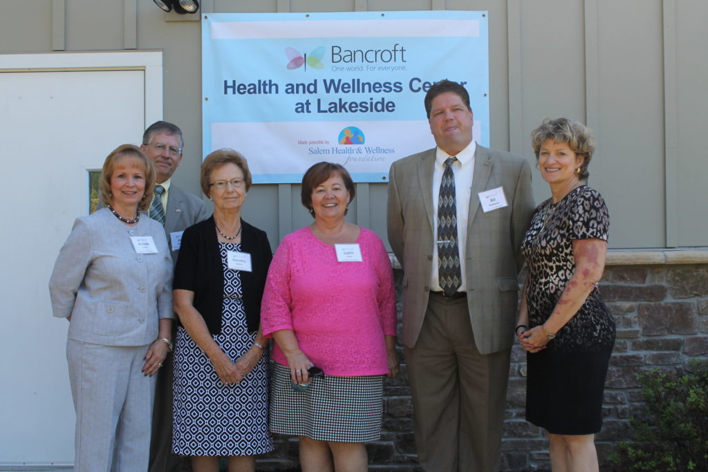 five Bancroft board members stand in front of a blue sign that reads "Health and Wellness Center at Lakeside" with the Bancroft logo and Salem Health & Wellness logo