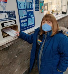 A light-skinned female and individual served casts her vote by dropping her voting ballot in the mailbox.