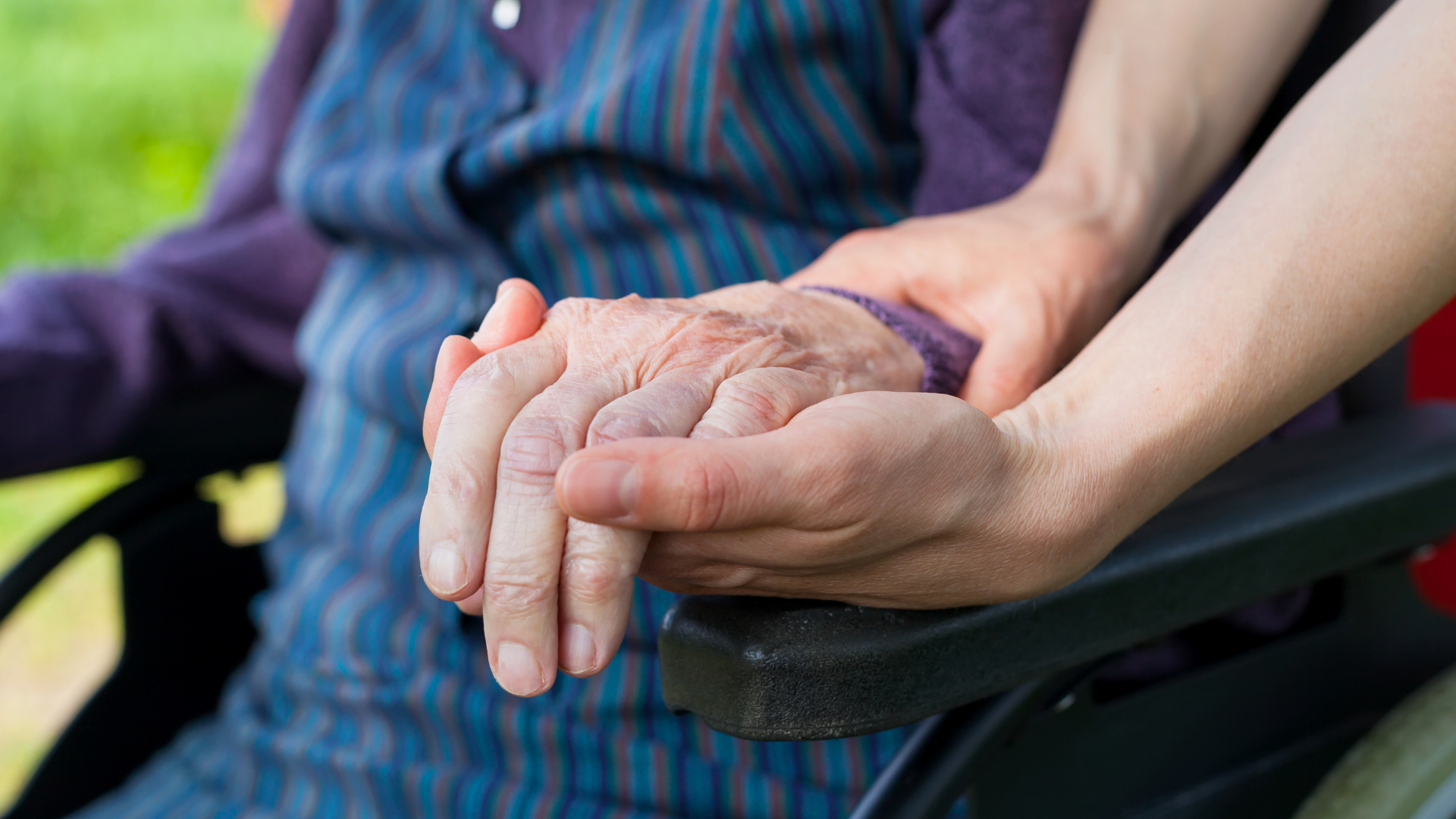 close-up photo of a person in a wheelchair's hand held by a paraprofessional's hand