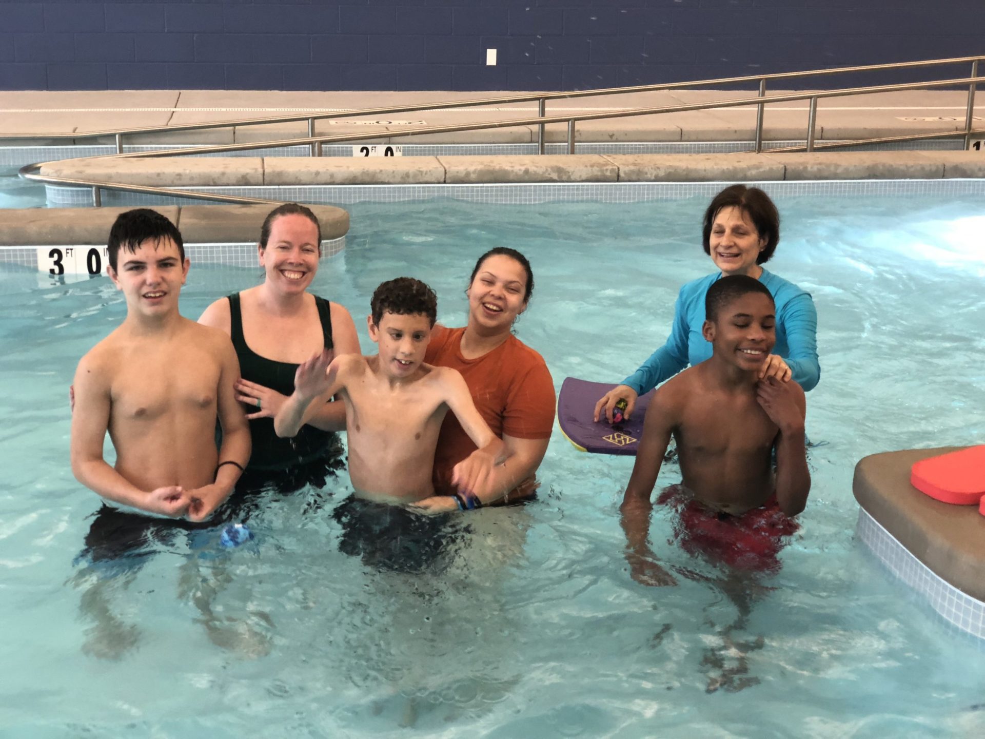six paraprofessionals and students stand in a swimming pool smiling