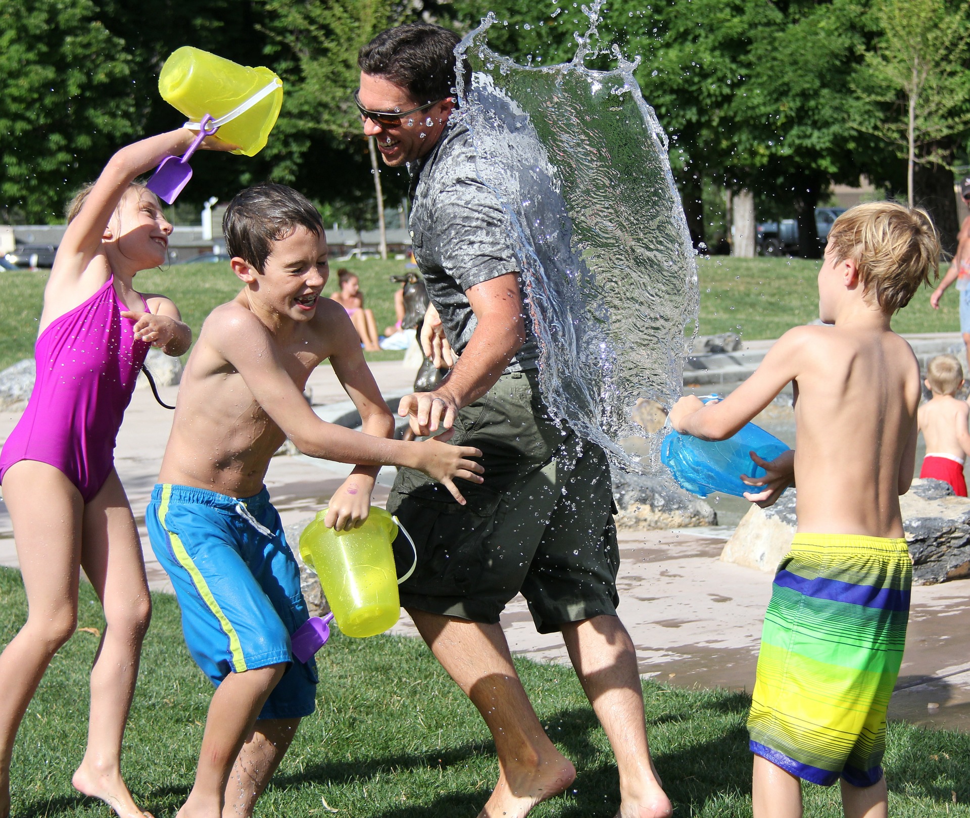 three children and a man in swimsuits use buckets to splash water on each other