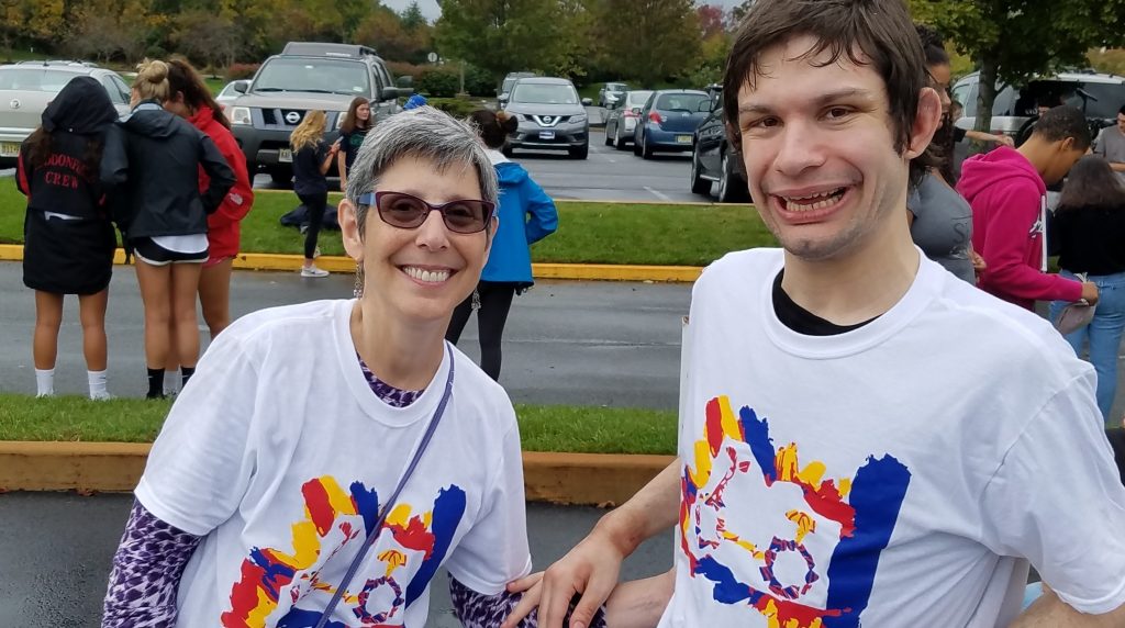 A mother and her adult son are wearing matching white t-shirts and are smiling at the camera. Her son is a resident in a Bancroft adult group home.