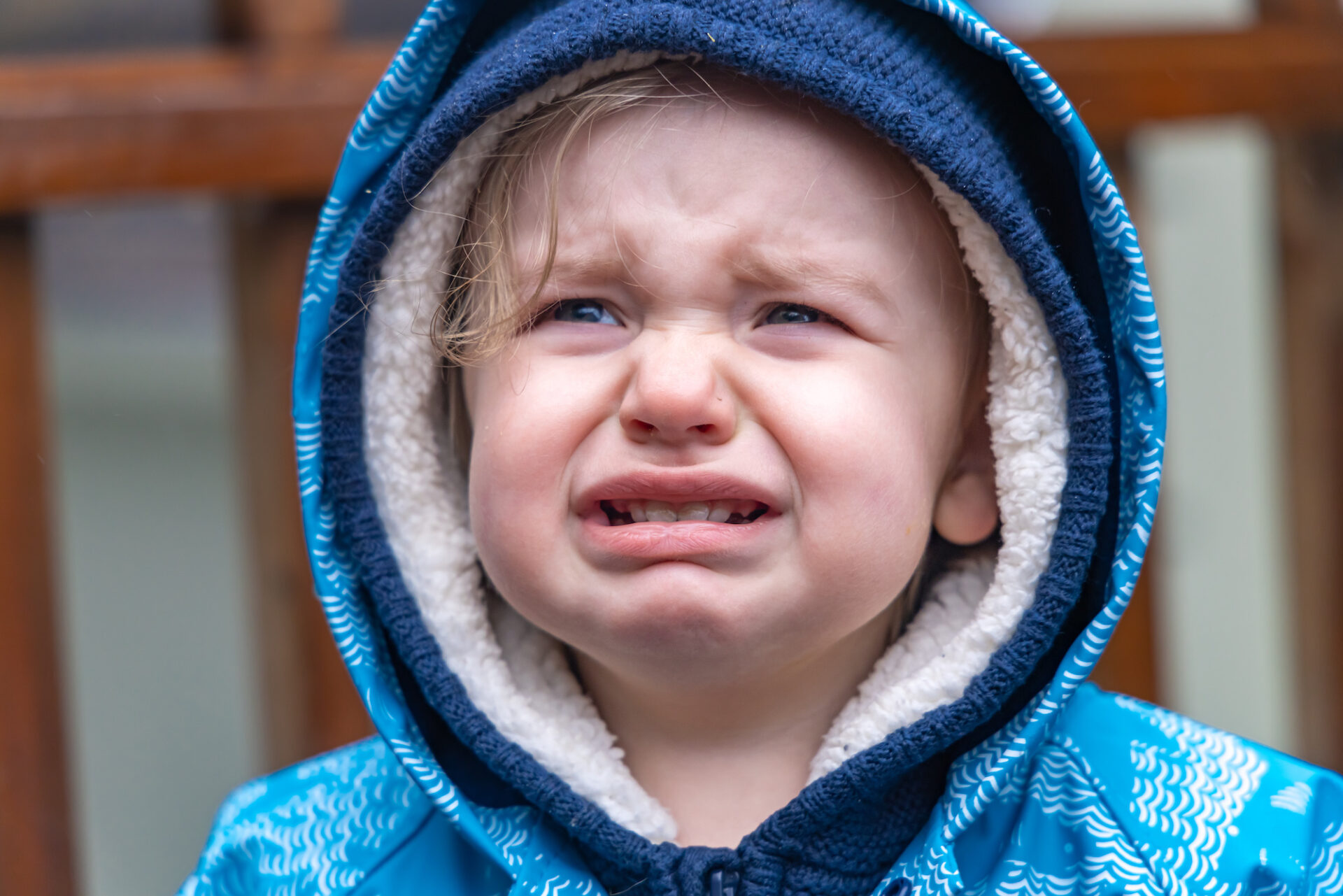 Little boy unhappy wearing blue hood outdoors.