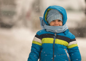 A small child is bundled up in a winter jacket. He is standing outside in the cold. 