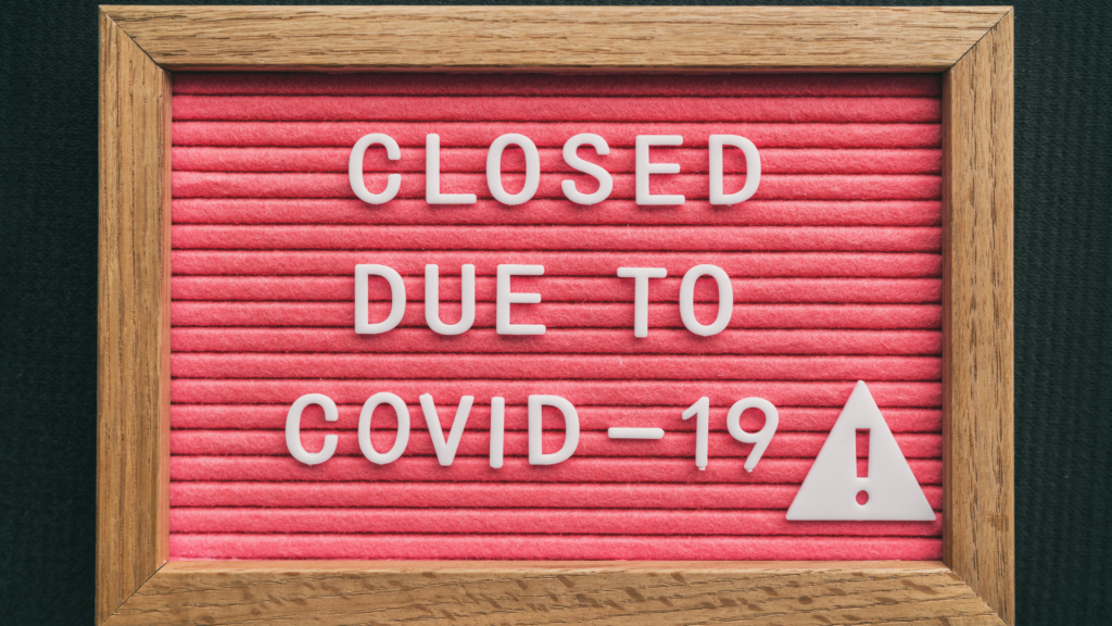 brown and red wooden sign that reads "CLOSED DUE TO COVID-19" with a caution sign in white letters