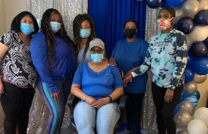 six women in blue shirts stand in front of a silver and blue sparkly background smiling