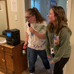 two young girls stand inside a house singing into a karaoke machine