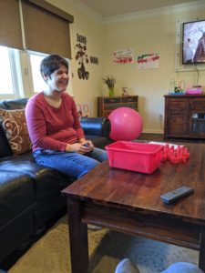 a woman in a pink shirt and blue jeans sits on a black couch at a wooden table playing a game