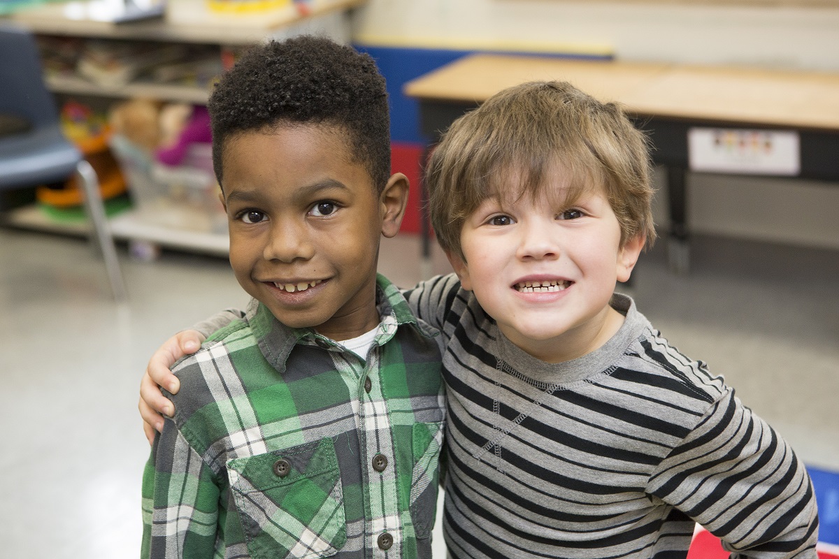 a young boy in a green plaid shirt and a young bow in a gray and black striped shirt stand together and smile