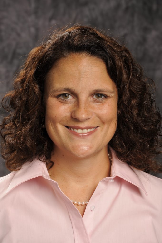 Kristin Vespe, a light-skinned woman with brown curly hair and a pink button down shirt, smiles