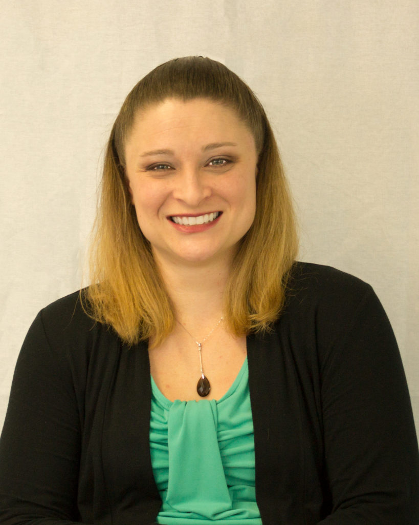 Misty Simmons, a light-skinned woman with shoulder length blonde hair wearing a teal top with a black sweater, smiles