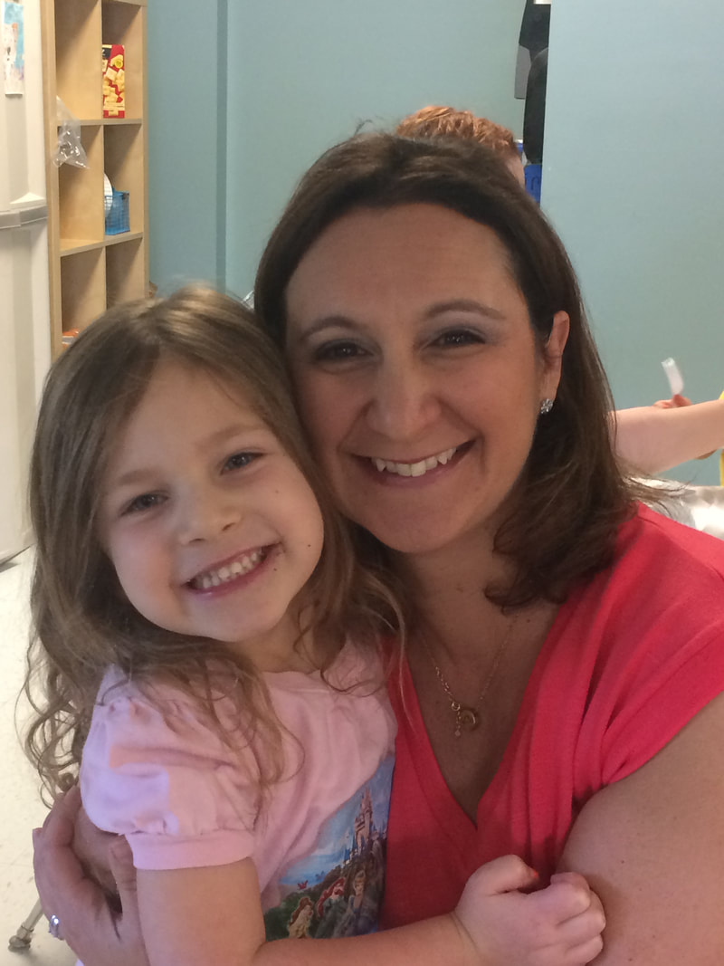 a woman and her daughter both dressed in pink tops with brown hair hold each other and smile