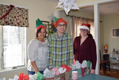three people wearing holiday-themed hats stand at a table full of presents