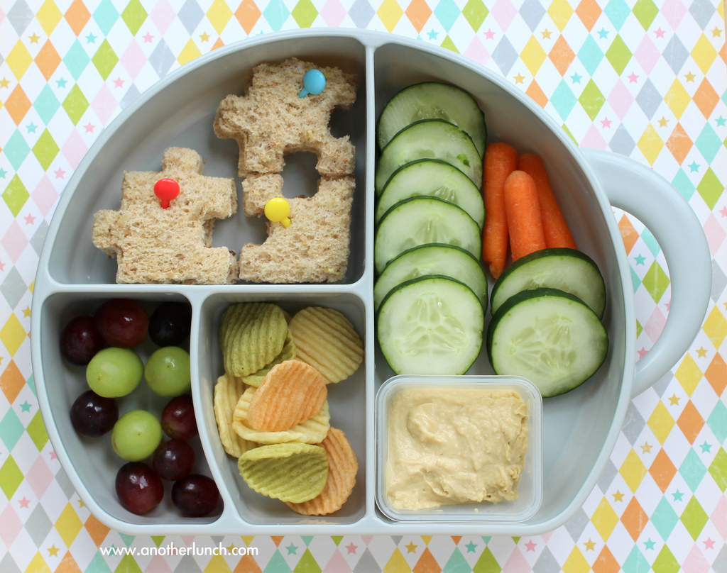 plate with bread, cucumbers, hummus, carrots, chips, and grapes