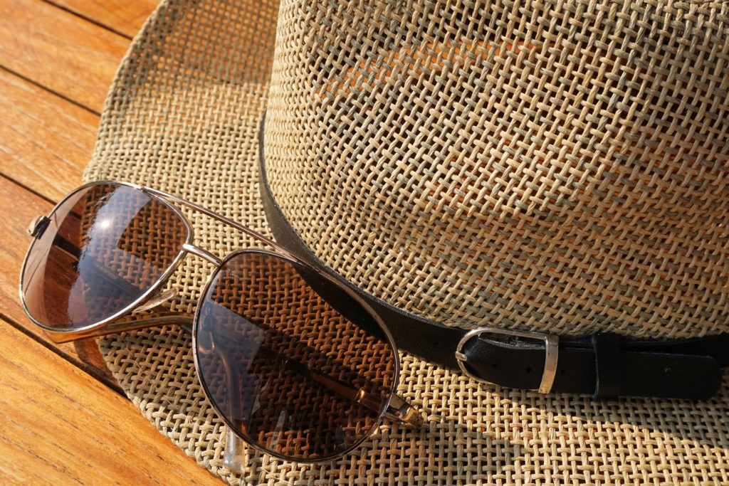 a pair of brown-shaded sunglasses sits on top of a tweed hat with a black belt around the rim