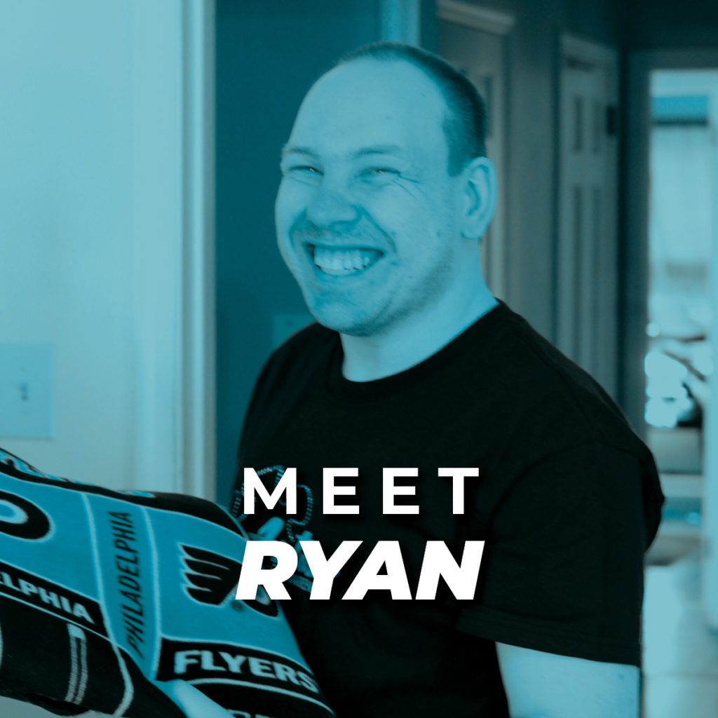 Ryan; a light-skinned man with short hair wearing a t-shirt and holding a Philadelphia Flyers towel