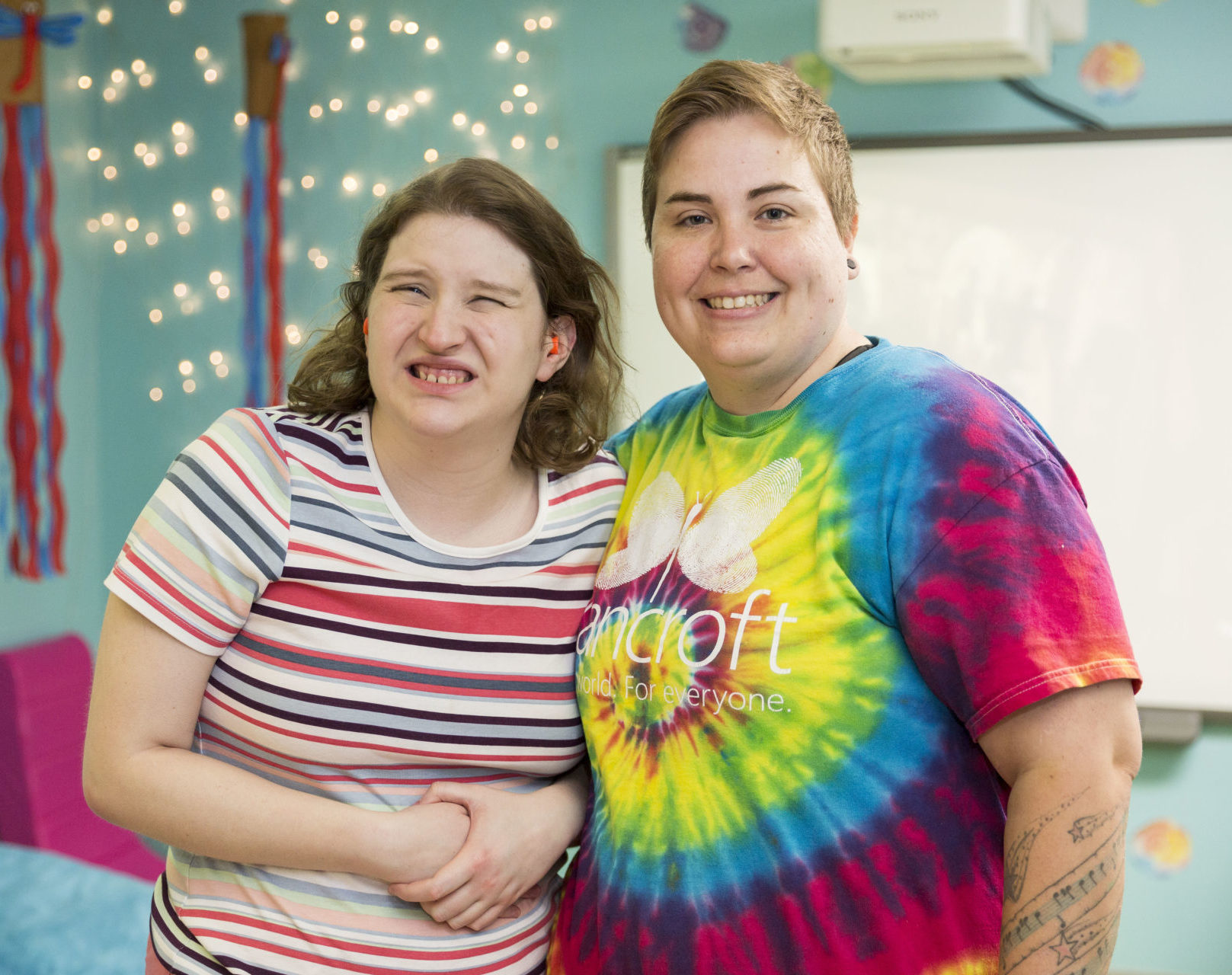 Bancroft Direct Support Professional standing with girl in a teal blue room.