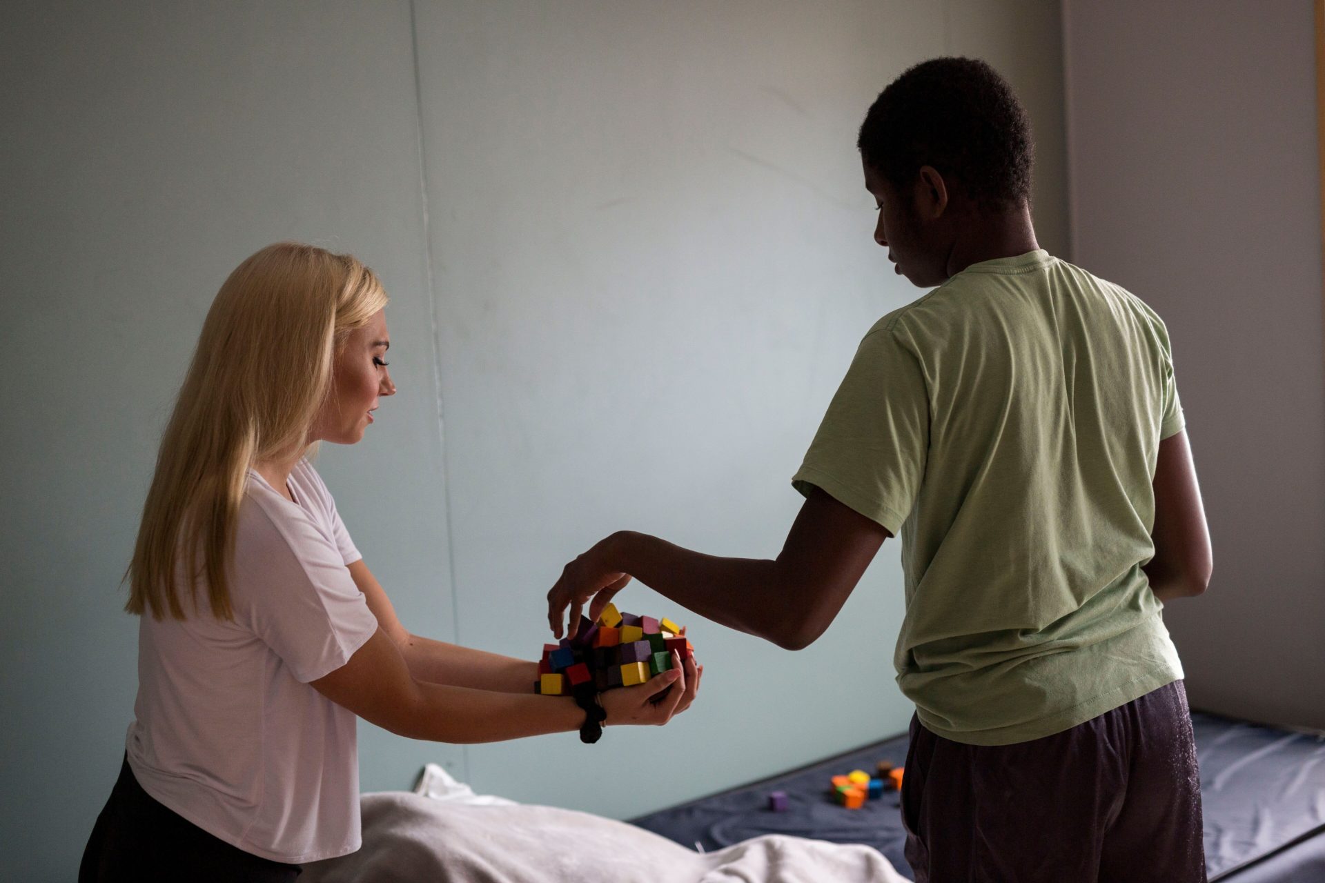 Bancroft Direct Support Professional cleaning up blocks in room with student