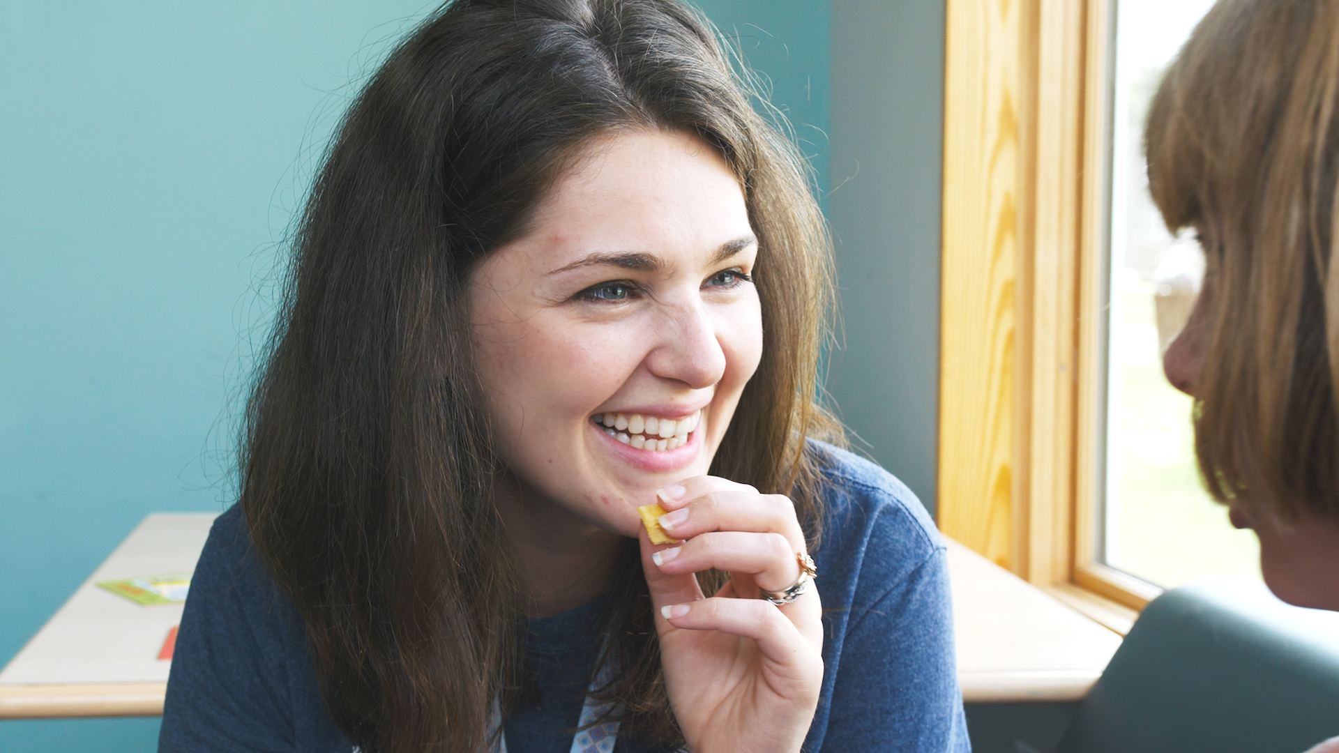 Adult woman in a blue shirt smiling and laughing while holding a small object in her hand