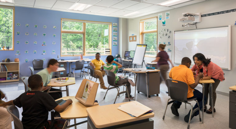 several students and Bancroft employees sit and stand in a classroom doing school work and talking