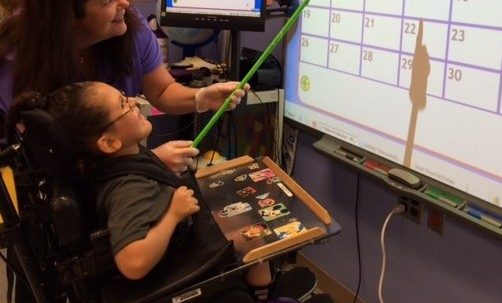 medically fragile child in wheelchair working with teacher at smartboard
