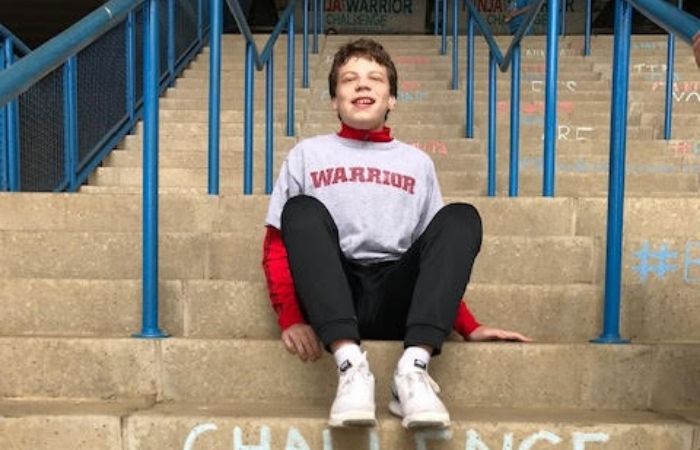 Young boy with brown hair sitting on steps outside.