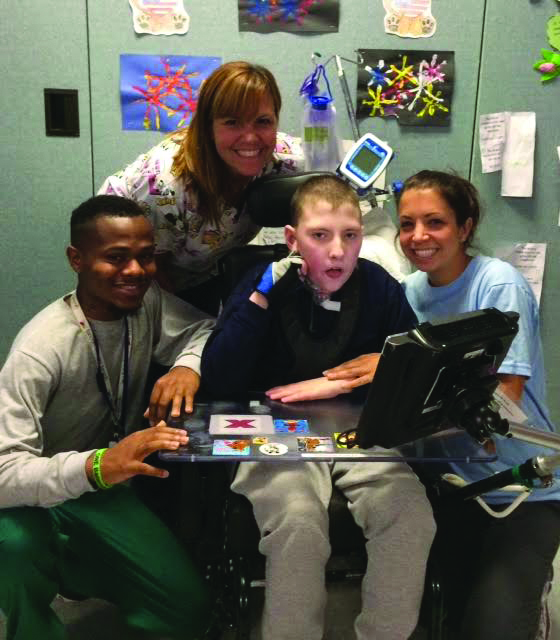 student in wheelchair with laptop surrounded by teachers and support staff