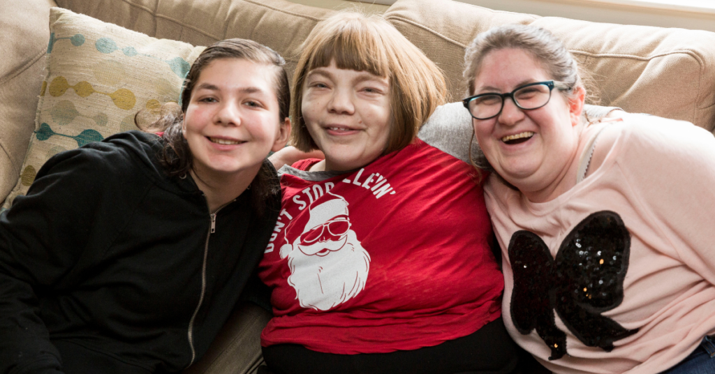 Three women sitting on a couch in their group home, smiling and posing for the camera.
