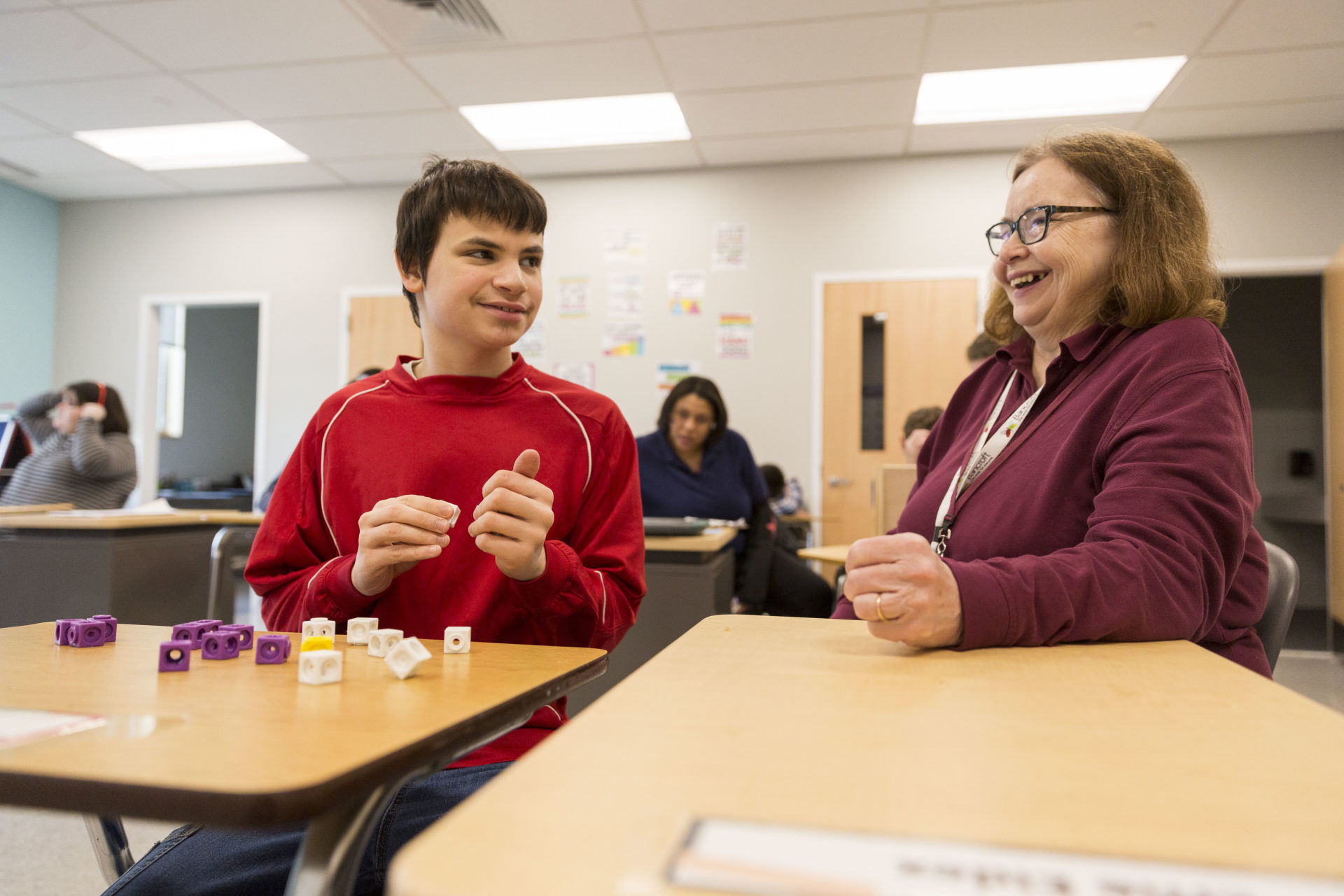 Paraprofessional sitting at desk laughing with student.