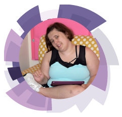 A young adult girl sitting in a pink chair wearing a sleeveless blut top. She is smiling at the camera