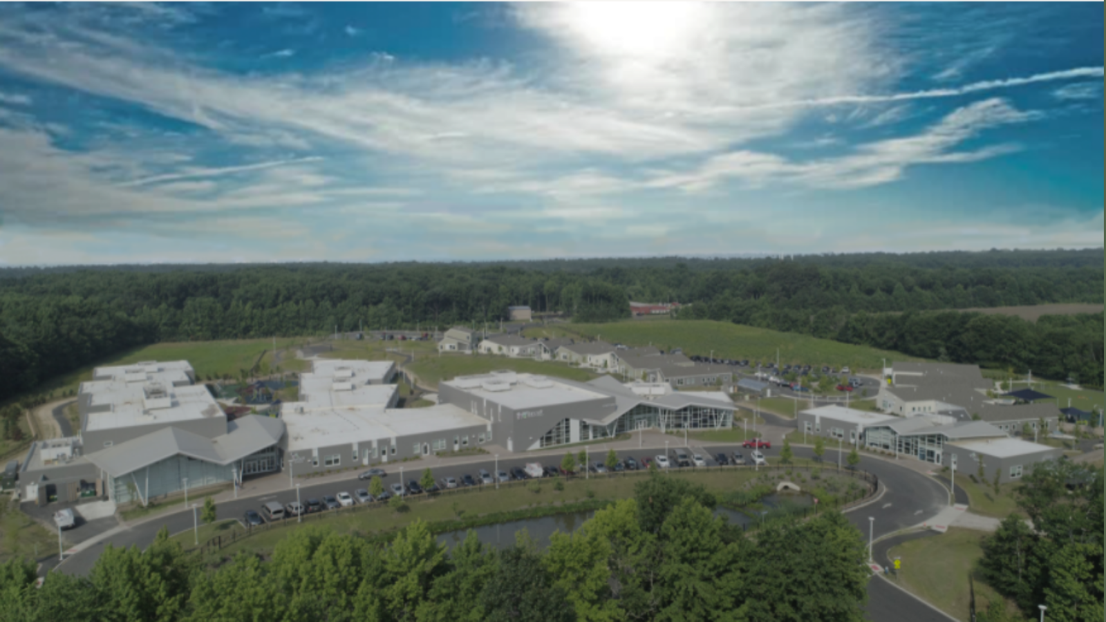 overlook of Bancroft's Mt Laurel campus; a group of grey buildings with white roofs and details in a semi-circle around a parking lot and green lawn