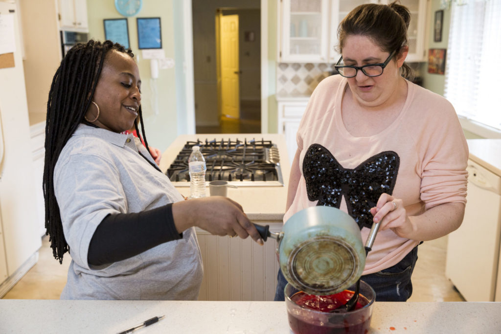 a female paraprofessional and a person served in a pink shirt with a black bow make red jam