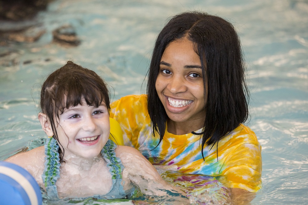 Child smiling in pool for swimming lessons with a paraprofessional