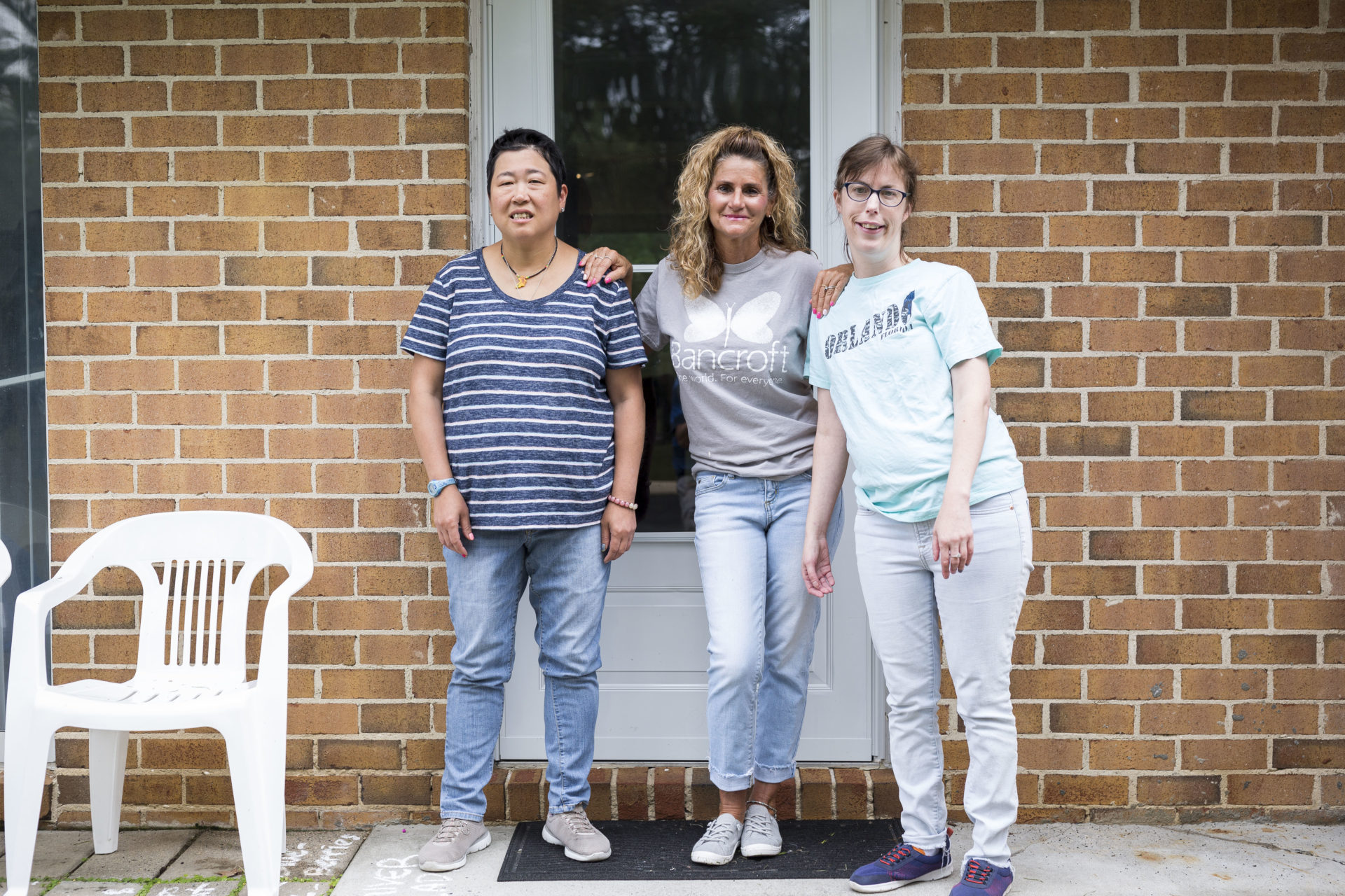 A paraprofessional in a gray Bancroft shirt stands with two persons served in front of a door on a brick building