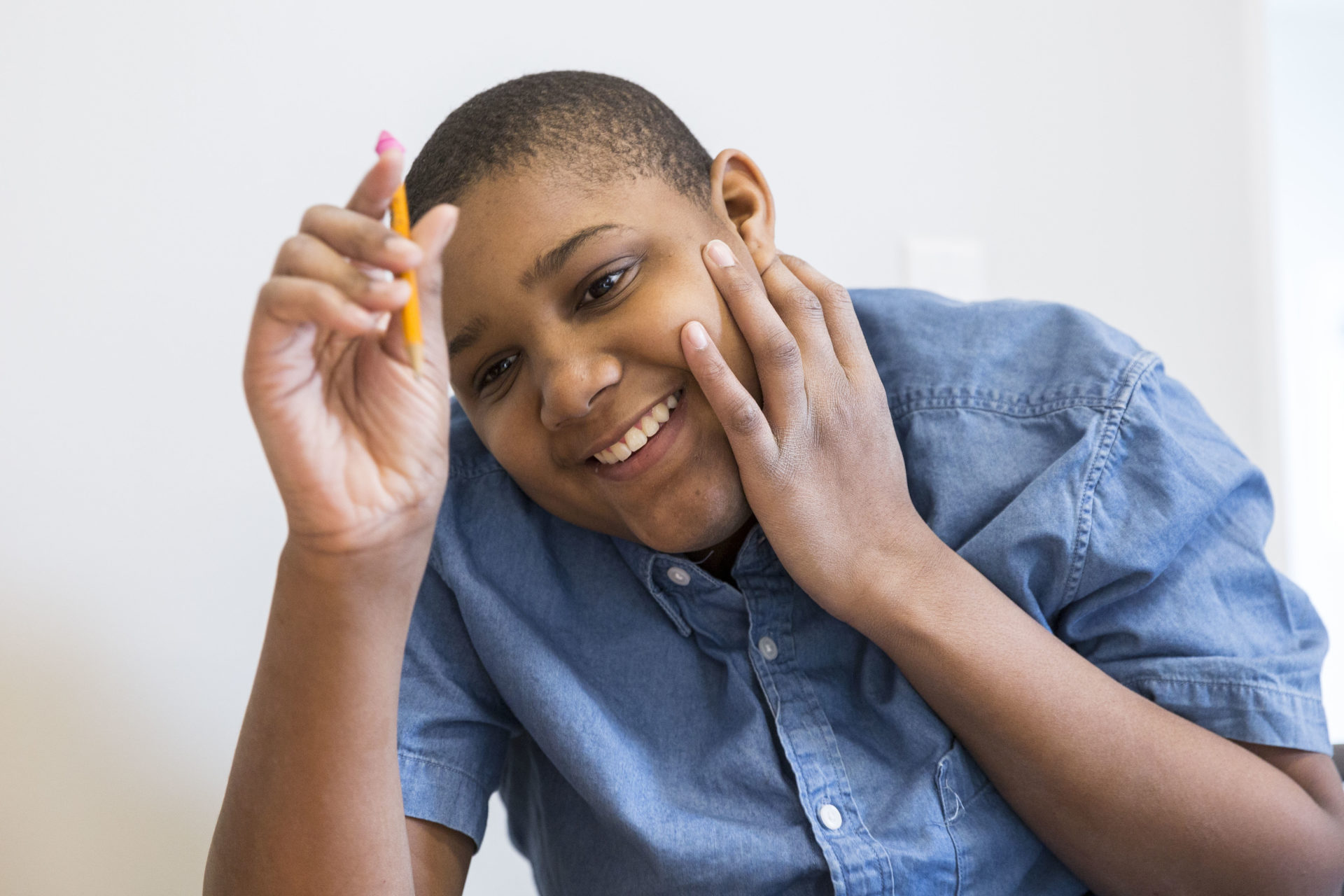 A light-skinned boy smiling at the camera holding a pencil.