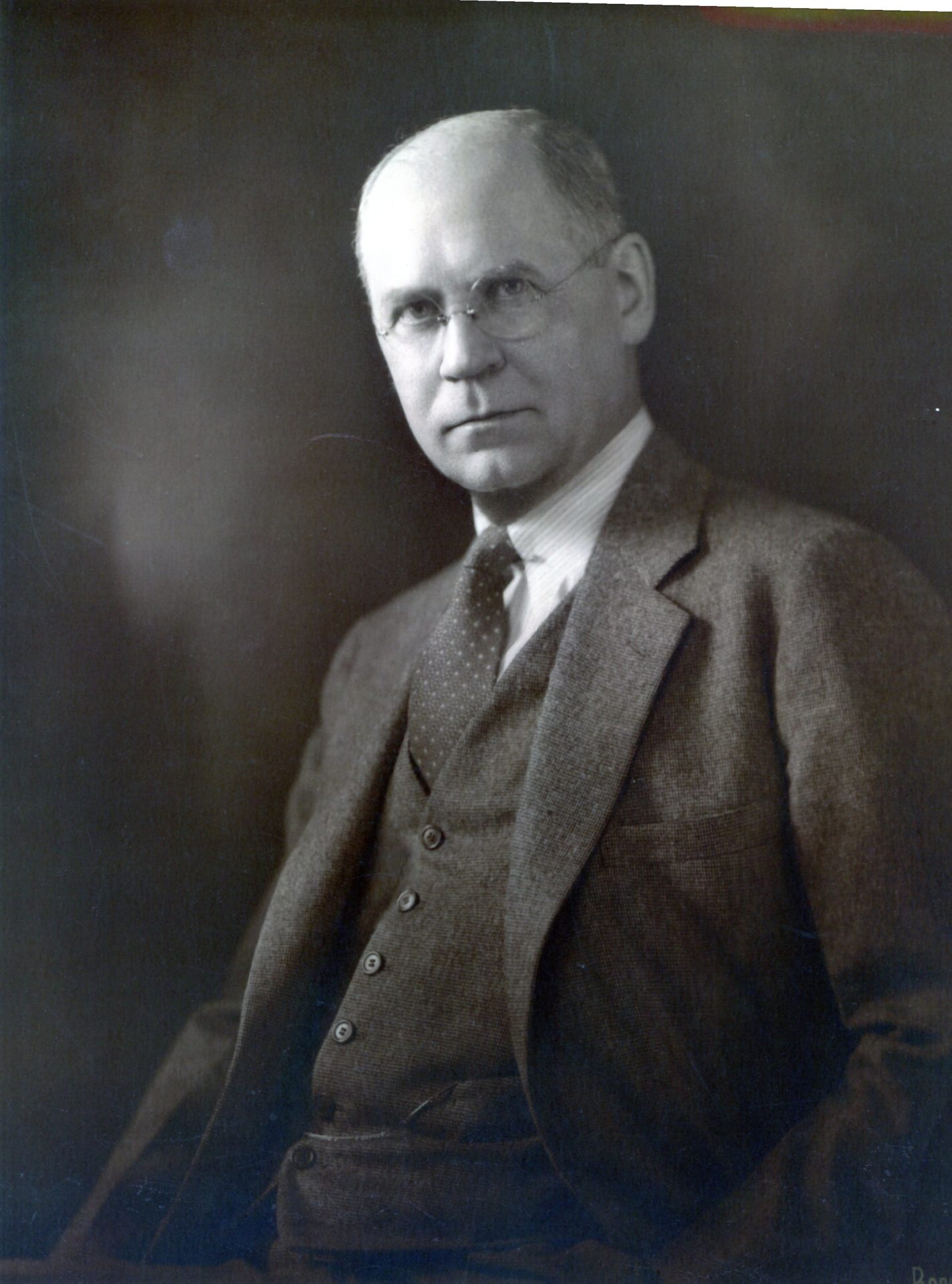 a black and white photo of a man with glasses wearing a suit and tie