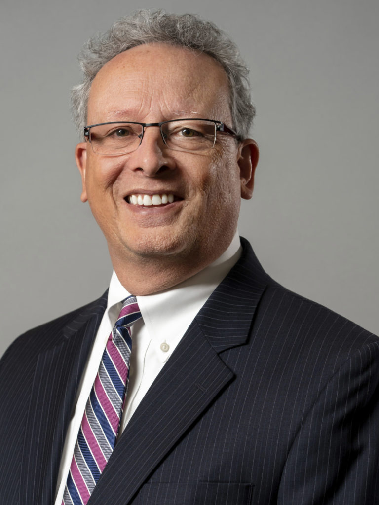 Light-skinned male in suit and tie smiling at the camera.