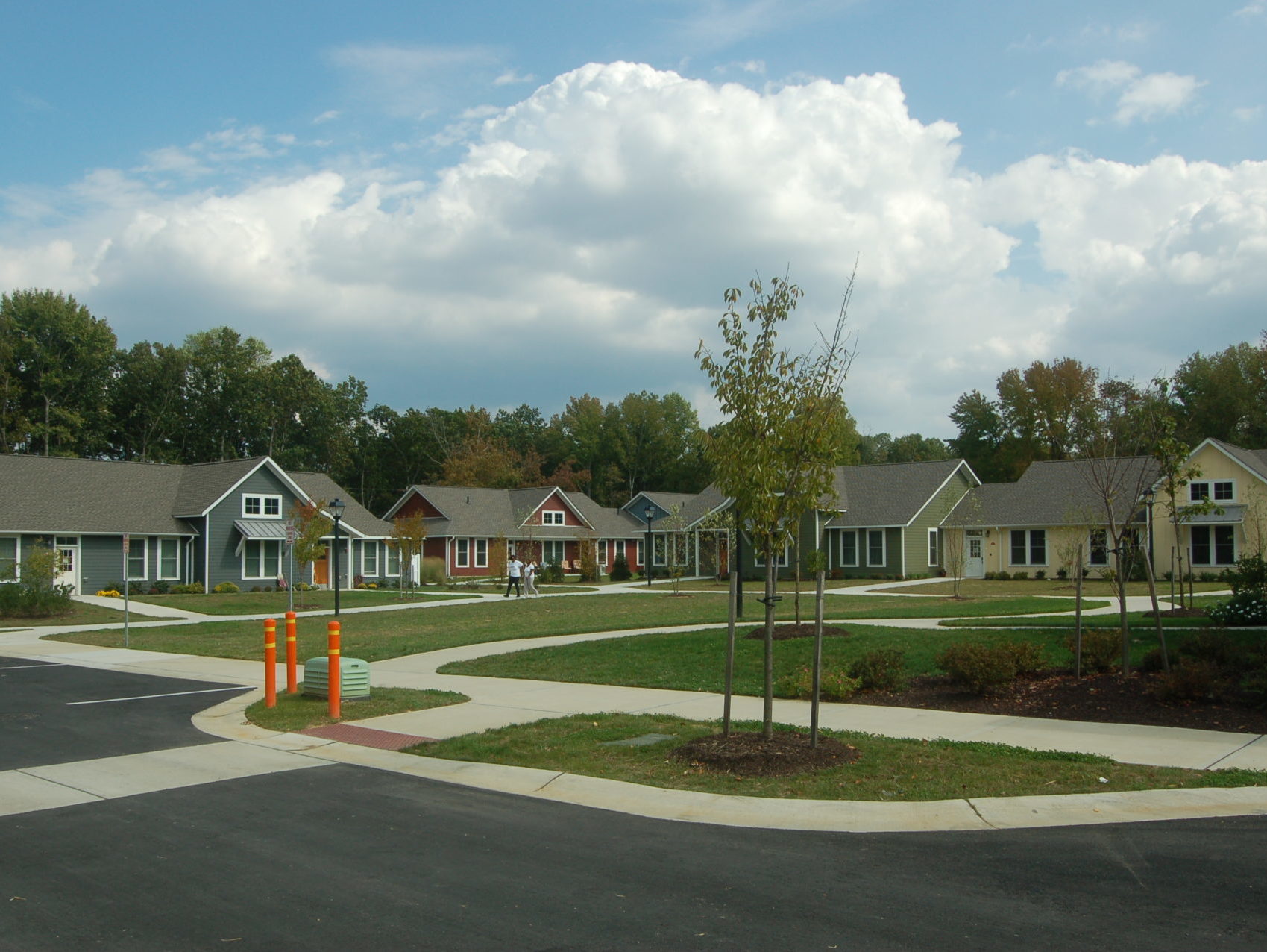 Four houses, two gray, one red, and one yellow, sit in a semicircle around a large green yard