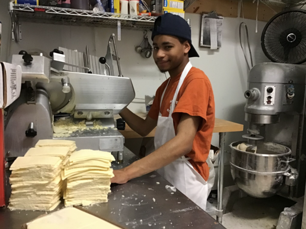 A young adult male is using a deli slicer to slice american cheese.