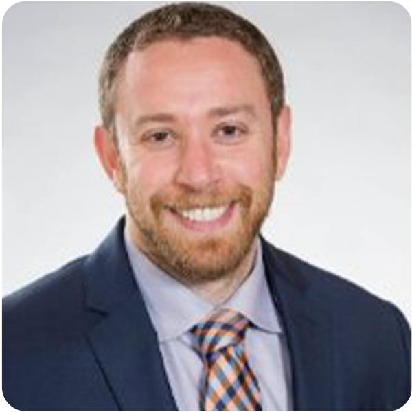 Avi Glickman, a light-skinned man with ginger hair and facial hair wearing a blue suit with a checkered tie, smiling