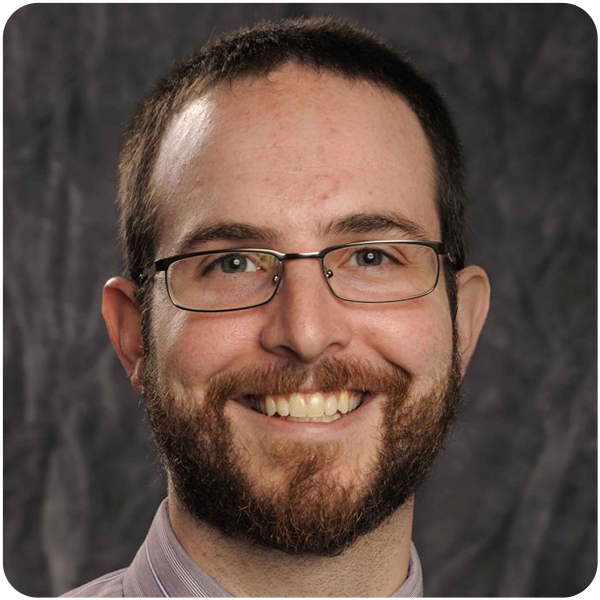 Nicholas Forvour, a light-skinned man with brown facial hair and glasses smiles