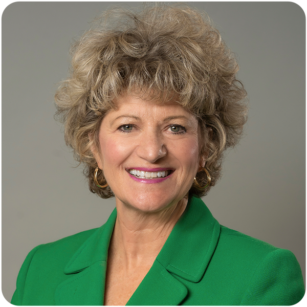 Toni Pergolin's headshot where she is smiling and wearing a green blazer jacket