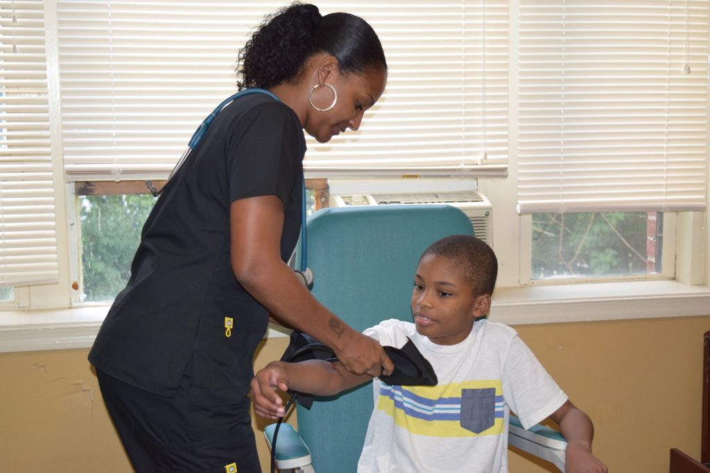 a female nurse in black scrubs puts a blood pressure cuff on a teenage boy