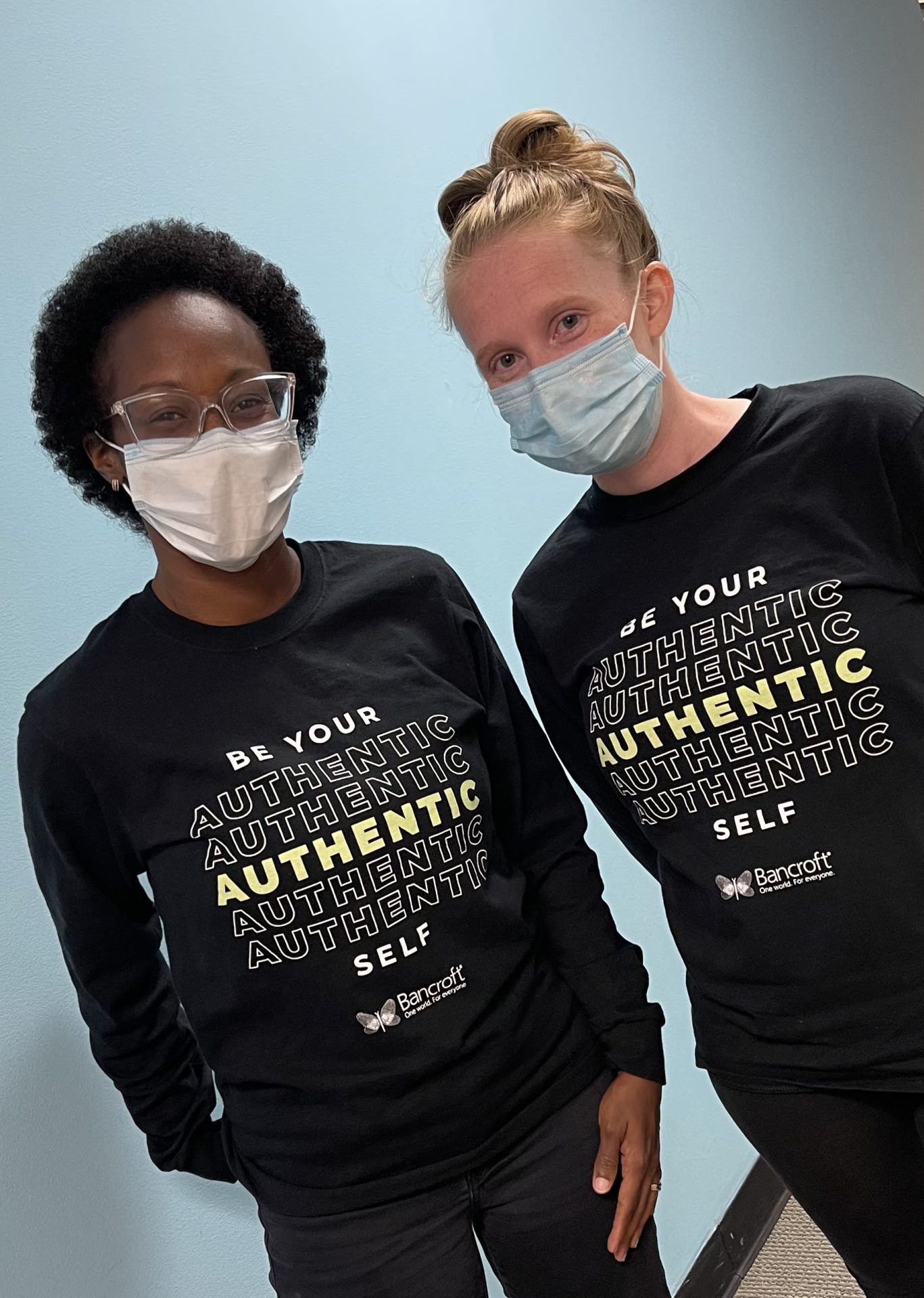 A dark skinned female stands with a ligh skinned female. they are wearing face masks and black long sleeve t-shirts.