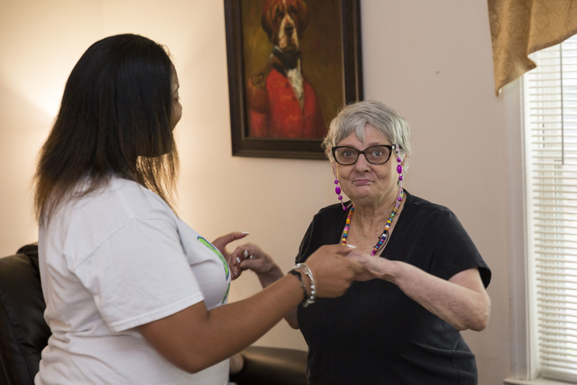 A dark skinned female is holding hands a dancing with a resident of the Flicker residences. The individual is light skinned and elderly.