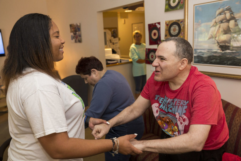 A dark skinned female is holding hands a dancing with a resident of the Flicker residences. The individual is light skinned and elderly.