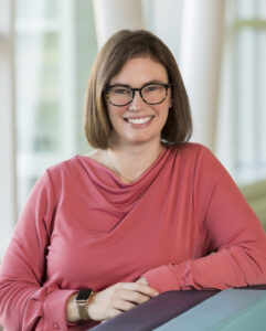 Dr. Danielle Ager, Psy.D. smiles and poses for the camera. She is in a salmon colored top and is wearing glasses.
