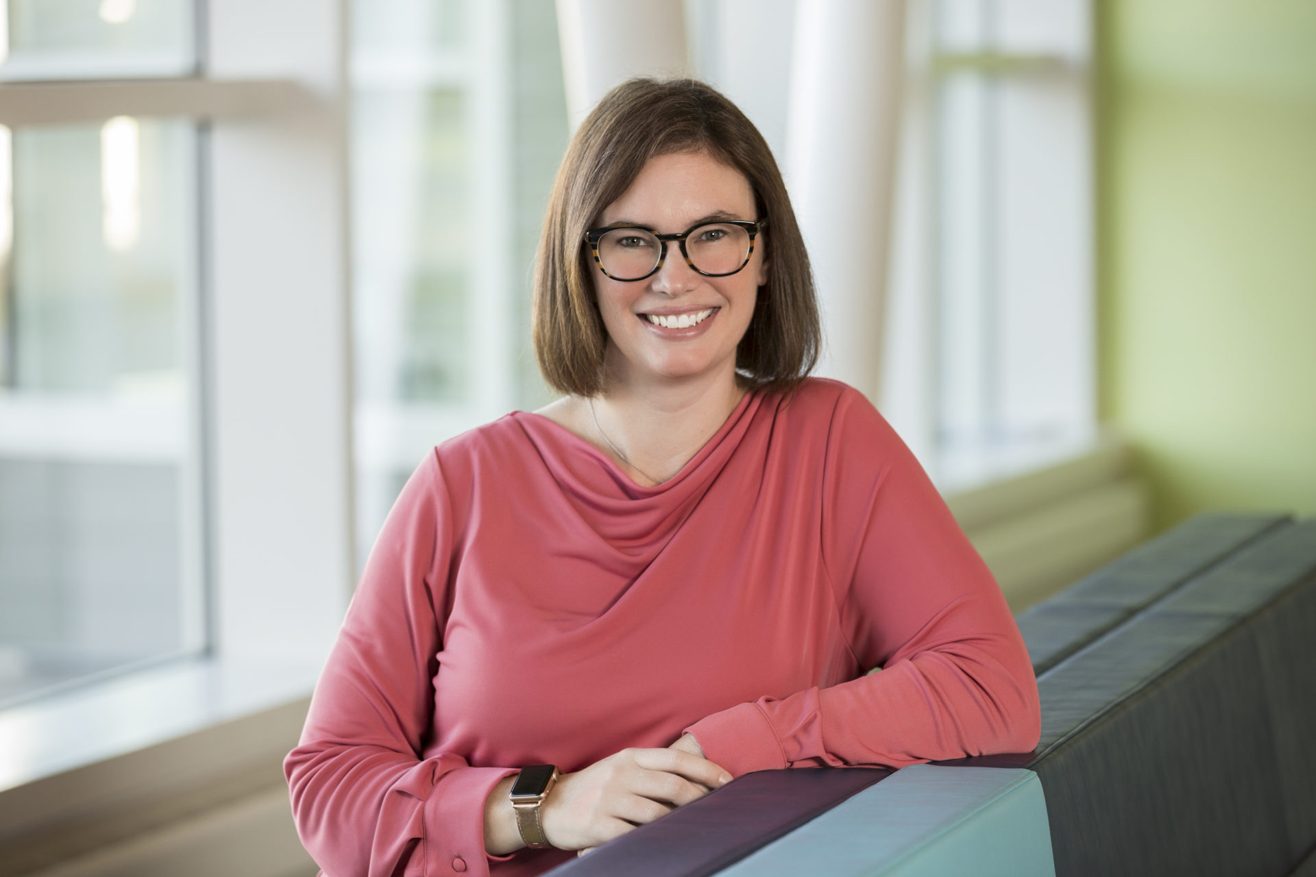 Dr. Danielle Ager, Psy.D. smiles and poses for the camera. She is in a salmon colored top and is wearing glasses.